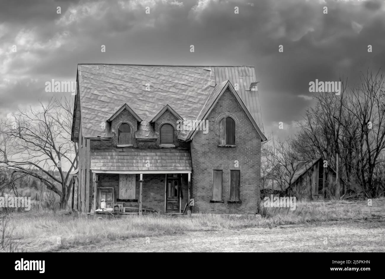 An old black and white abandoned spooky looking farmhouse in winter on a farm yard in rural Canada Stock Photo