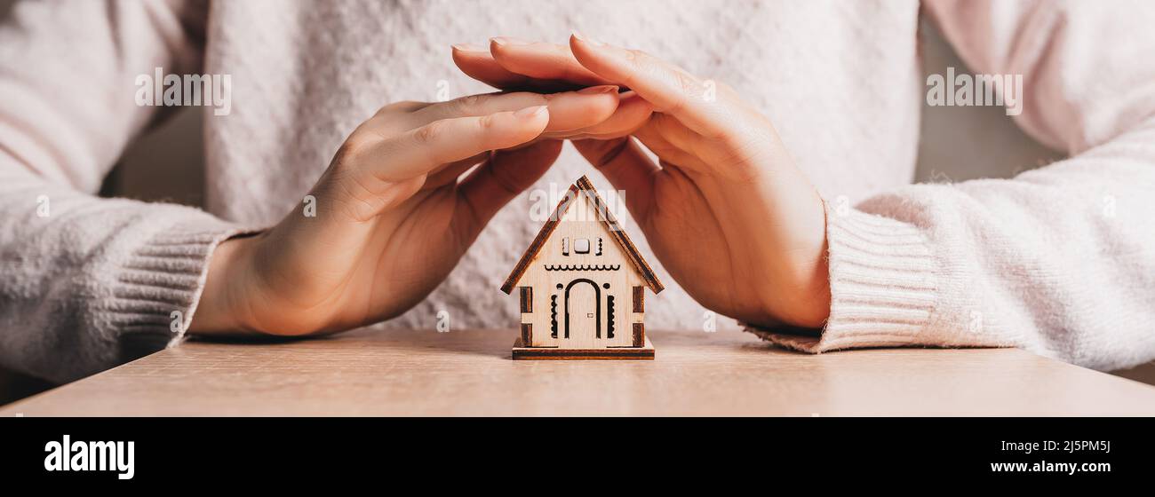 Woman holds and protects a wooden house with her hands with the sun on ...