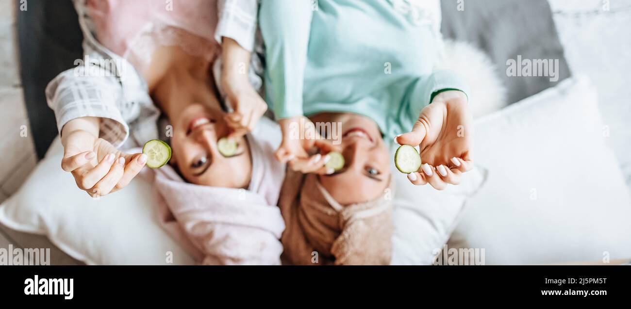 Two girls make homemade face and hair beauty masks. Cucumbers for the freshness of the skin around the eyes. Women take care of youthful skin, friends Stock Photo