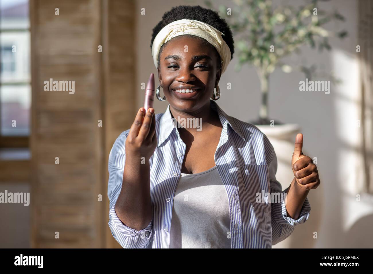 Contented african woman in light clothes holding mascara Stock Photo ...
