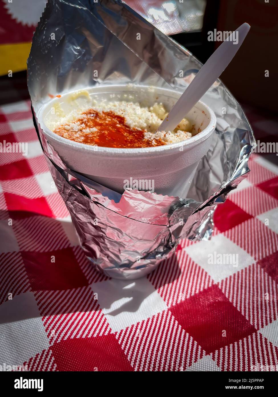 Styrofoam coffee cup with plastic spoon and used creamer container in  foreground and human elbows on table in background. Stock Photo