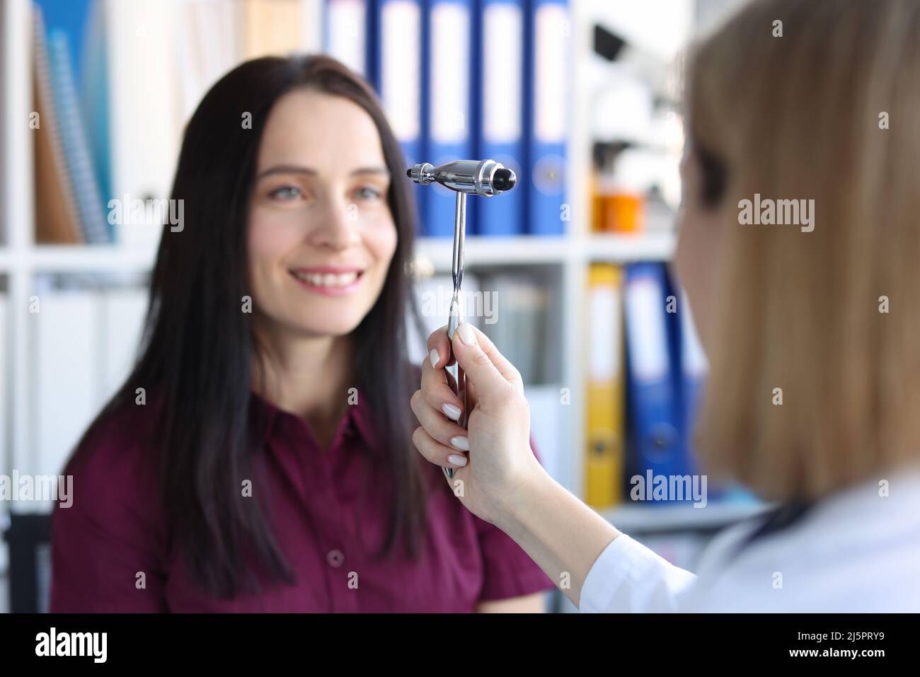 Neurologist doctor driving hammer tool in front of patient eyes in clinic Stock Photo