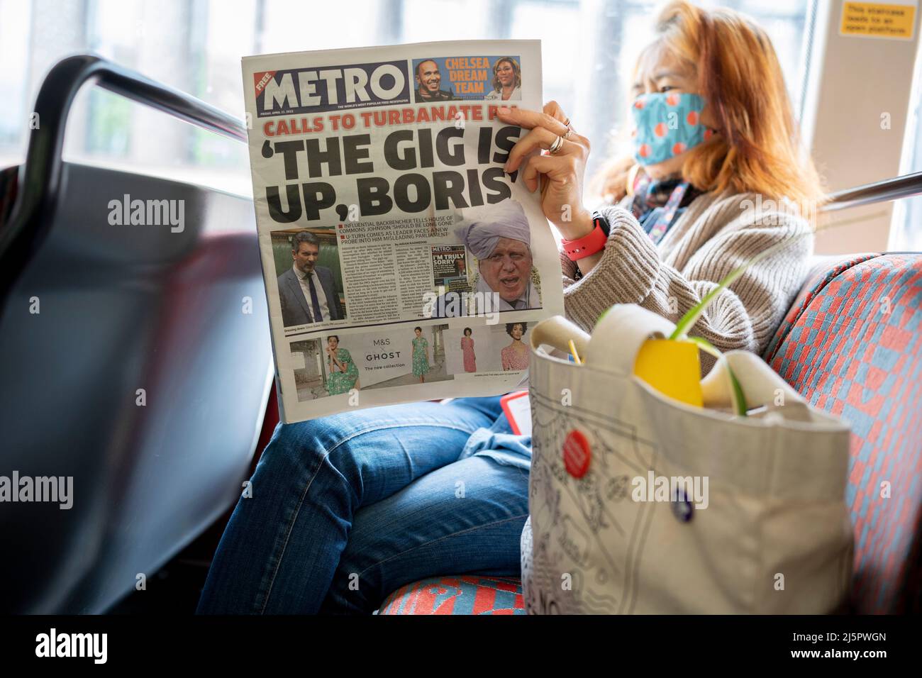 A woman bus passenger reads her copy of Metro newspaper whose front page headline is about the scandal of UK Prime Minister Boris Johnson's fine for partying during the Covid pandemic, when his own rules for gatherings were forbidden, on 22nd April 2022, in London, England. The quote 'The Gig Is Up, Boris' refers to Conservative MP Steve Baker in parliament, telling Johnson (currently in India) that he should resign. More Fixed-Penalty fines for illegal parties in volving Johnson in Downing Street are expected to be issued by the Met police. Stock Photo