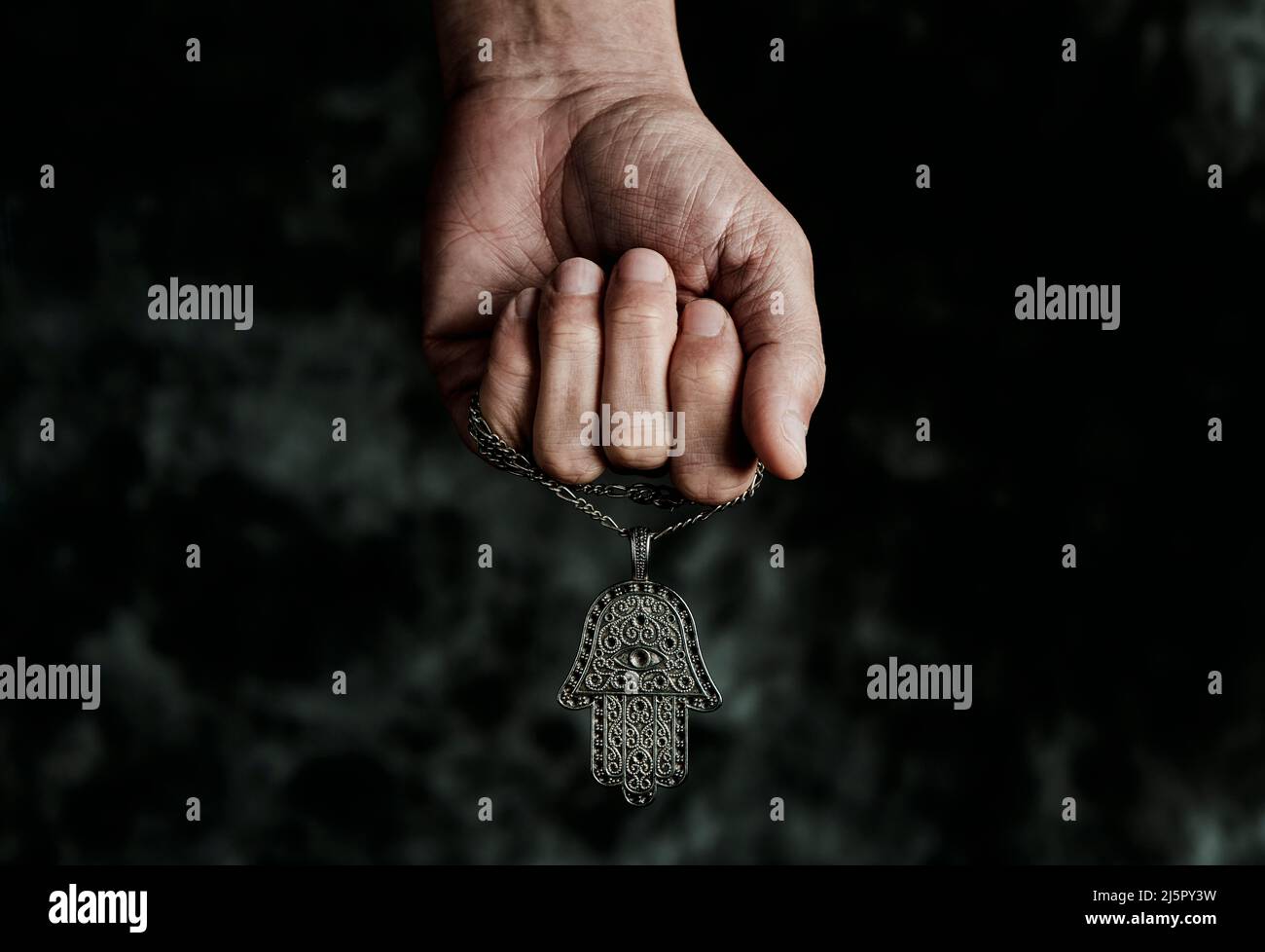 a man is holding an old hamsa amulet, also known of the hand of fatima or the hand of mary, on a black mottled background Stock Photo