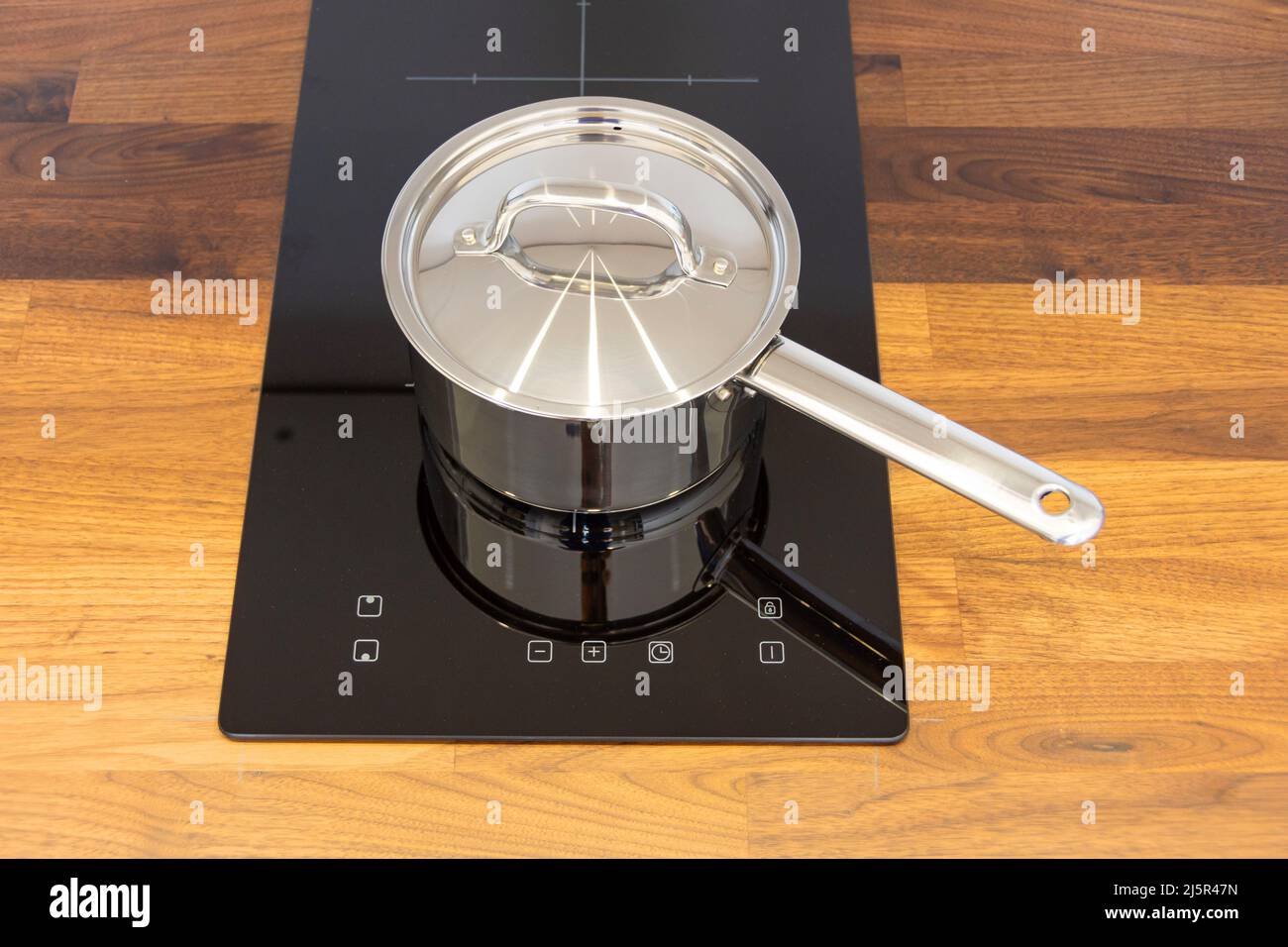 Saucepan ladle with lid on an induction hob built into a wooden kitchen