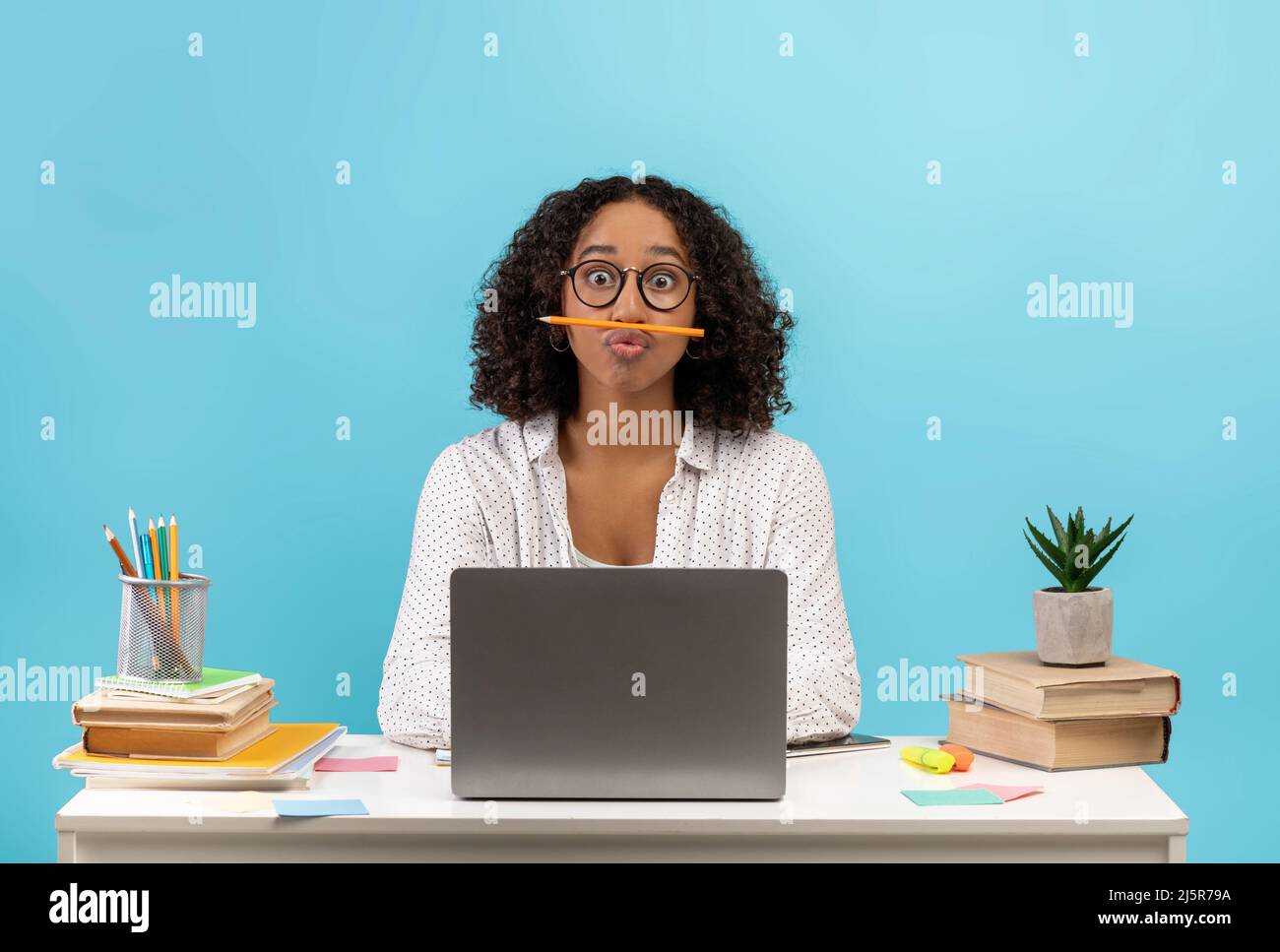 Silly young black female student sitting at desk with books and laptop ...