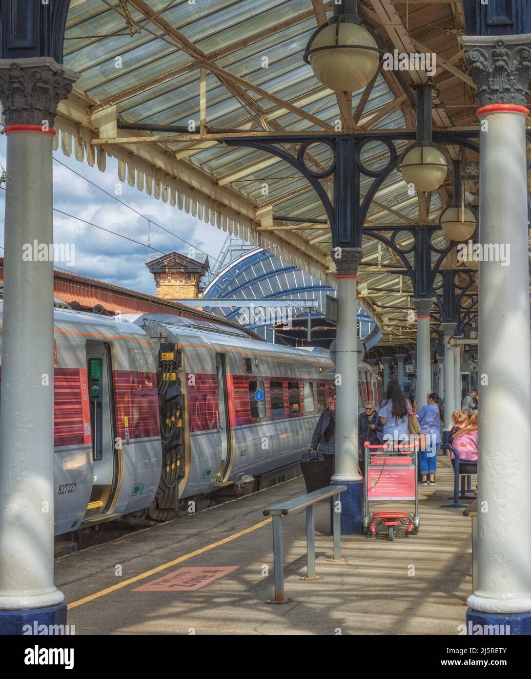 Train Columns Passengers wait beside train carriages on a historic platform with ...