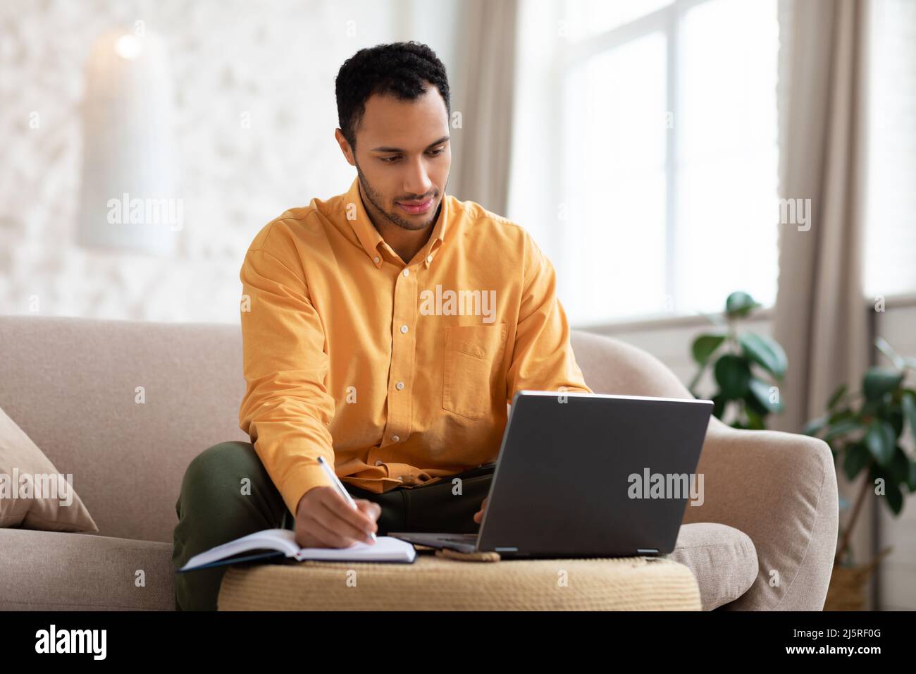 Portrait of focused Arab man using laptop and writing Stock Photo