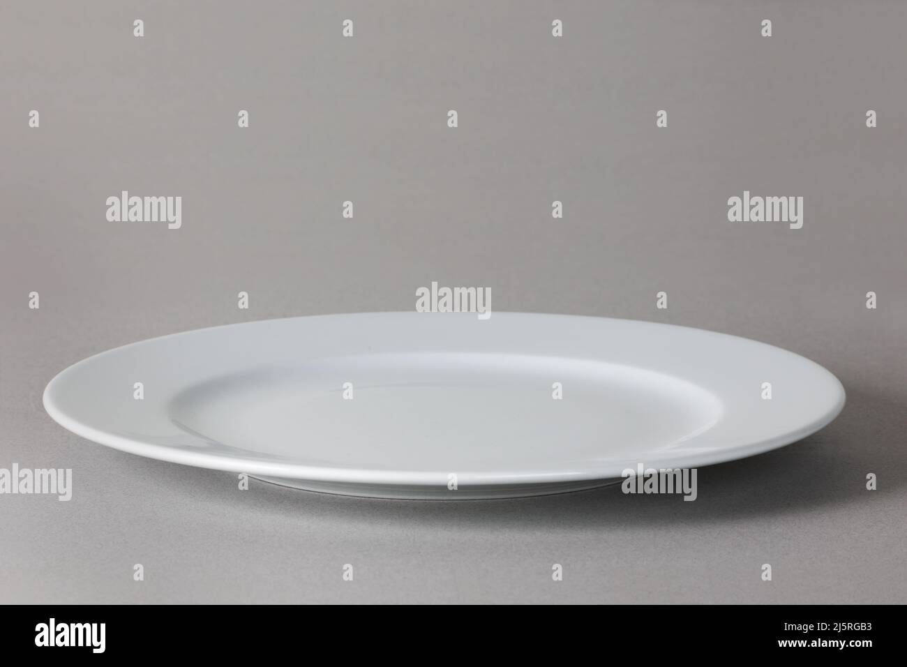 Flat front angle view of a white dinner plate on neutral background with shadow Stock Photo