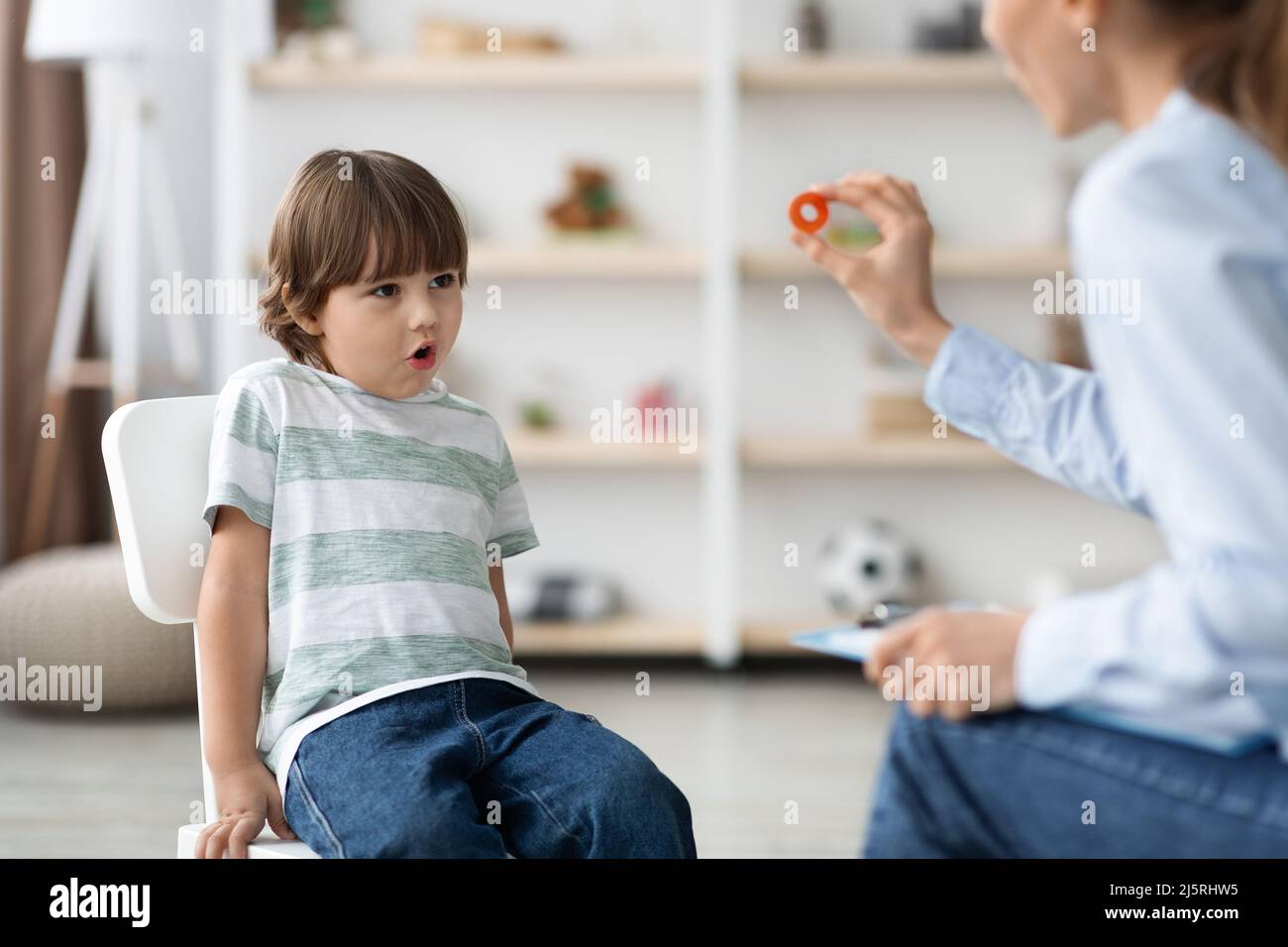 Cute little boy studying with professional woman speech therapist, pronouncing sound O at classroom Stock Photo