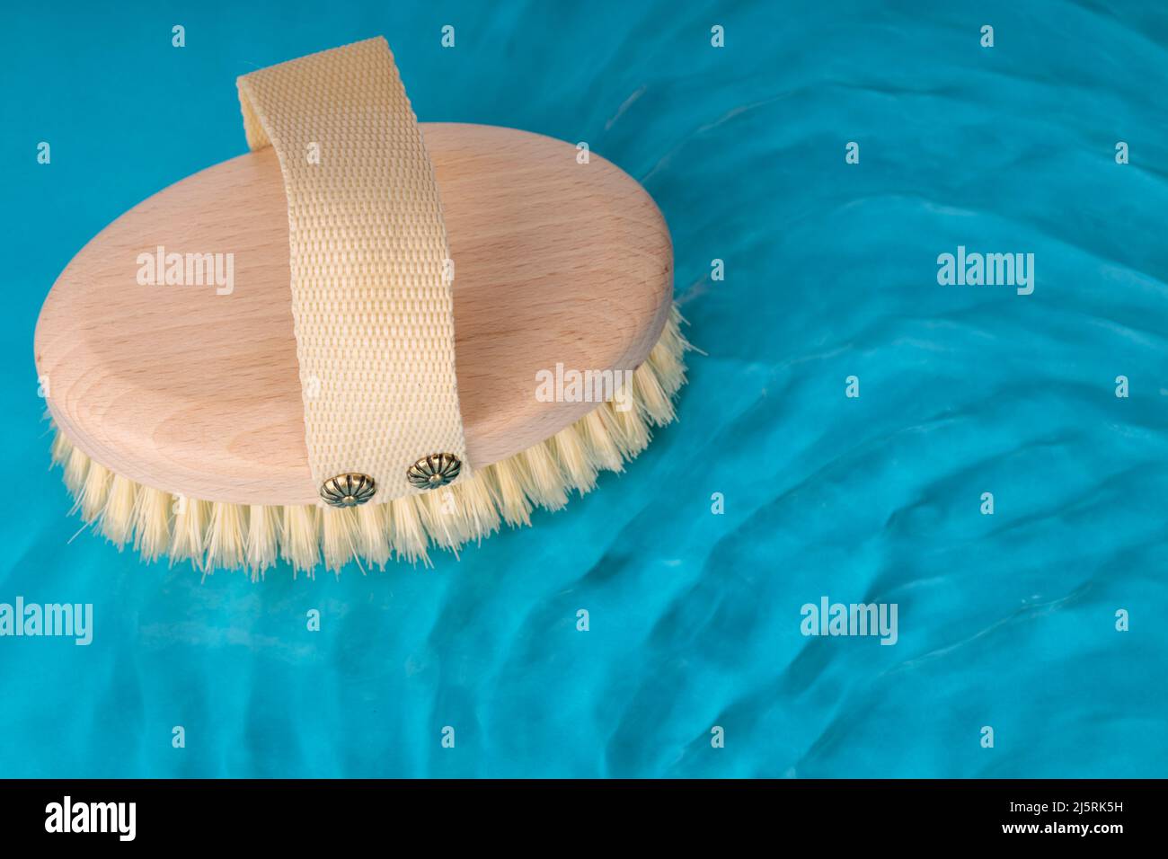 Natural wooden brush for brushing dry body against background of blue water. Top view Stock Photo
