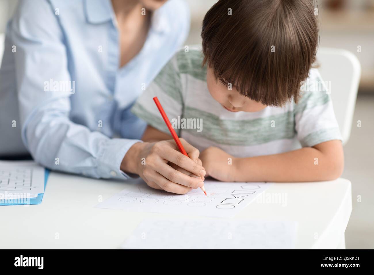 Early development training. Concentrated little boy pupil painting with teacher at kindergarten, free space Stock Photo
