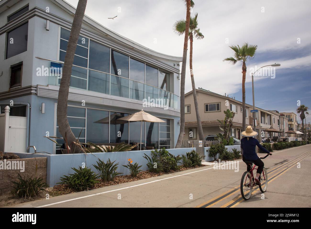 Woman riding a bicycle in front of some summer holiday houses, Ocean front Walk, Mission Bay, San Diego Stock Photo