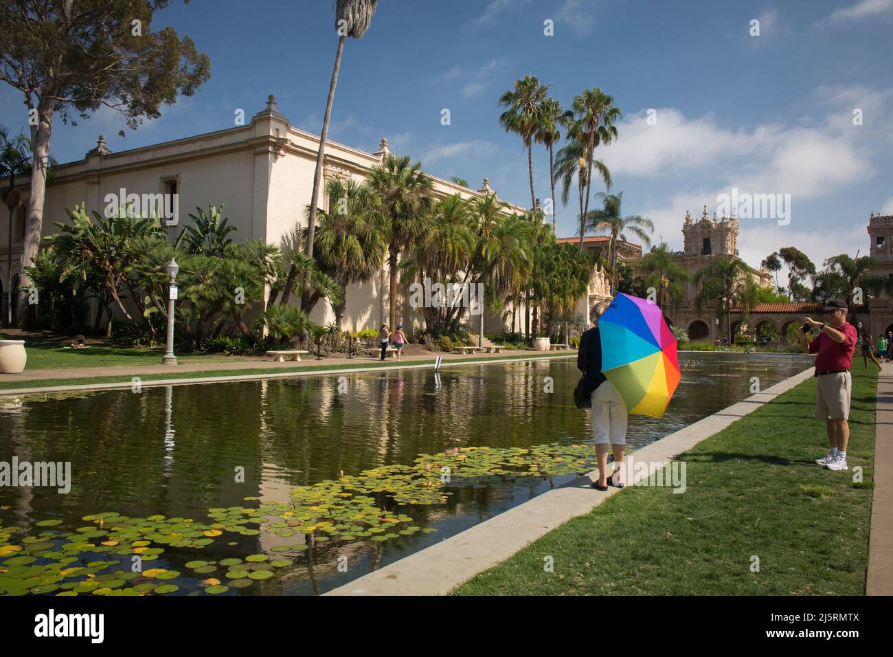 Tourist taking a photo of his wife with a colorful umbrella by the Balboa Park Lily Pond and Lagoon, San Diego Stock Photo