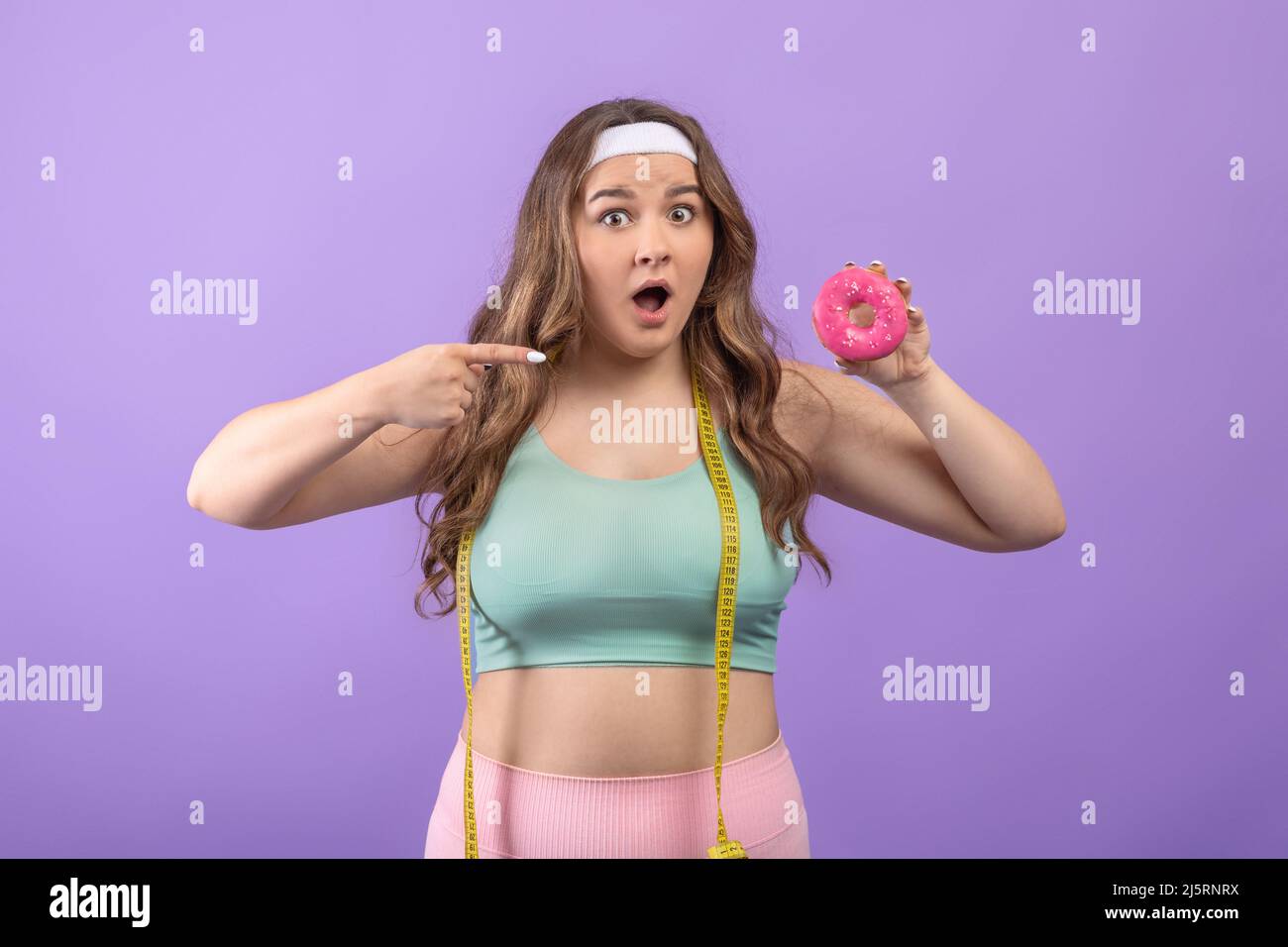 Surprised hungry young european plus size lady with open mouth points finger at donut in hand Stock Photo