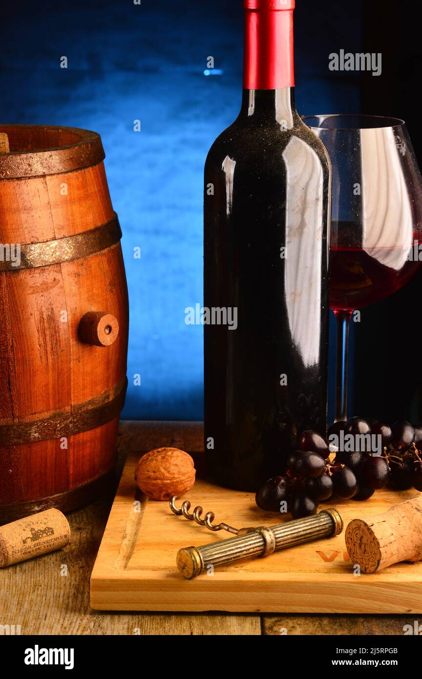 Still life with glass and bottle of wine.A barrel and corc nerb.background:dark blue gradient . Stock Photo