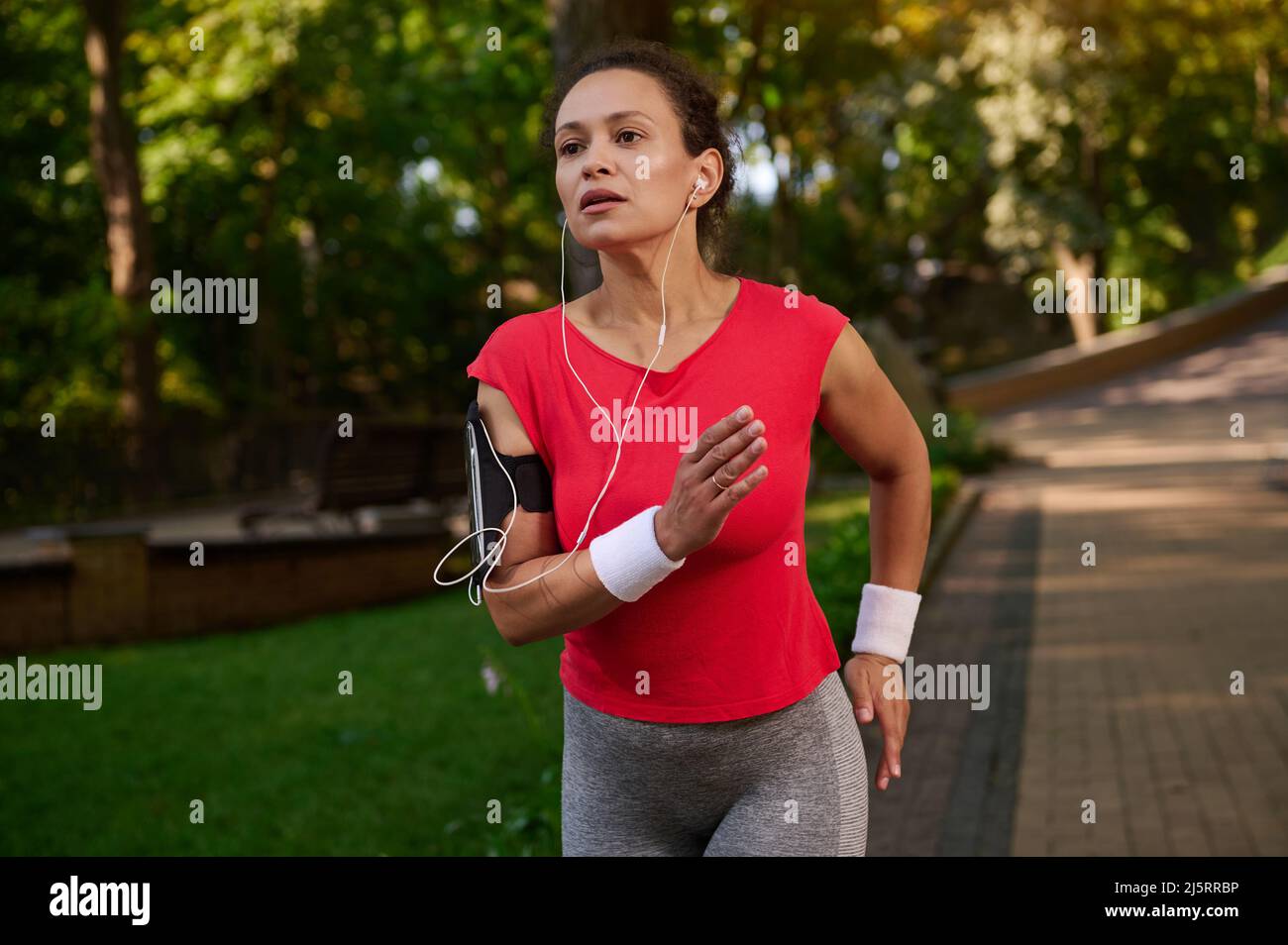 Stunning attractive exhausted strength muscular Hispanic sportswoman, athlete, runner with healthy beautiful aesthetic fit body runs on city park foot Stock Photo