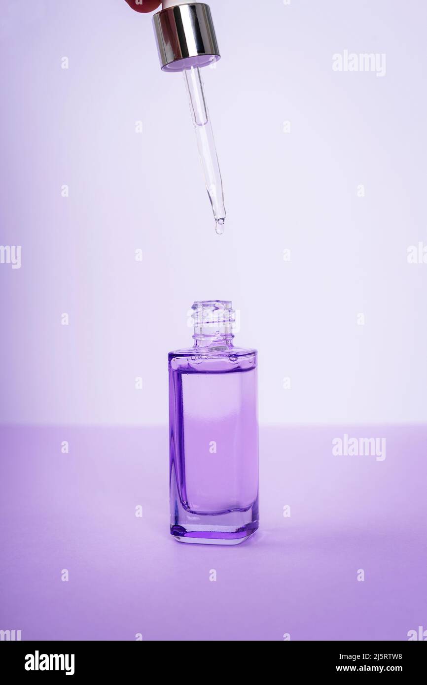 Bottle of cosmetic serum with pipette on purple background. Trendy selfcare products. Front view. Stock Photo