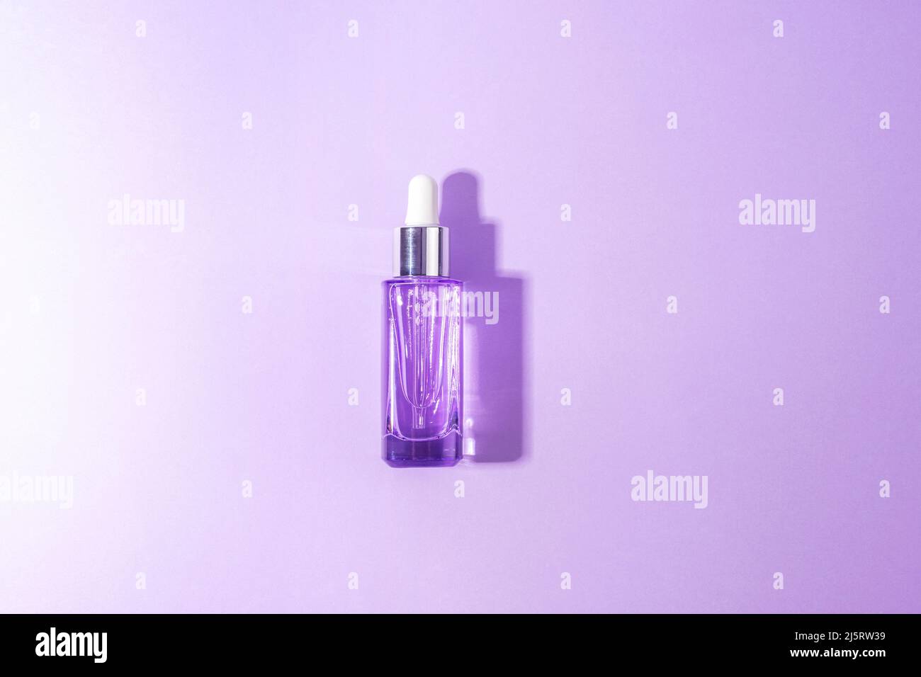 Cosmetic serum bottle with hard shadows on light purple background. Trendy selfcare products. Top view, flat lay. Stock Photo