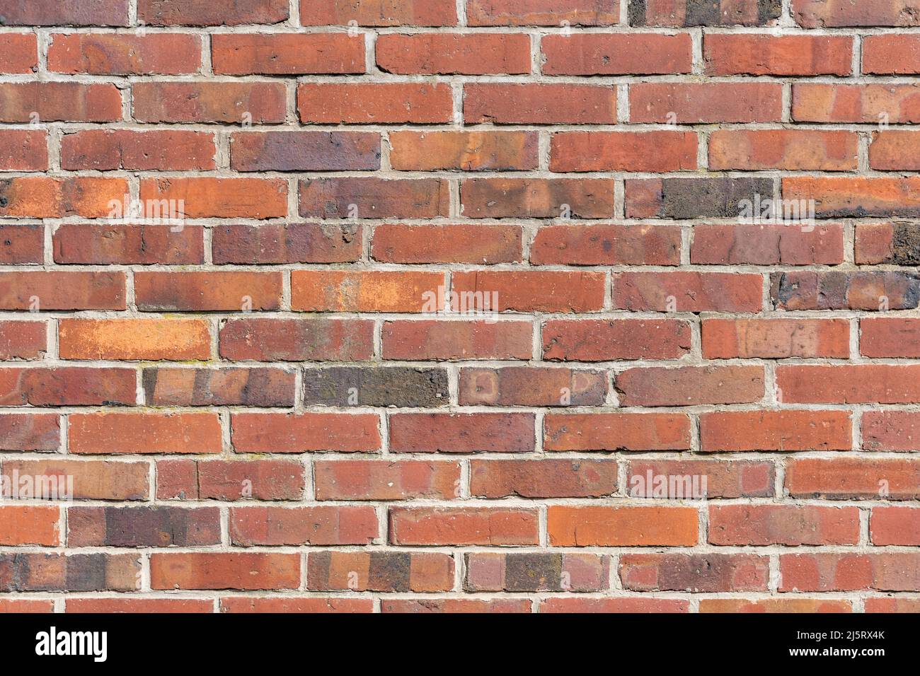 Red brick wall background texture. Multiple rows of weathered stone blocks. Full frame backdrop of a building facade. Rough exterior of a house. Stock Photo