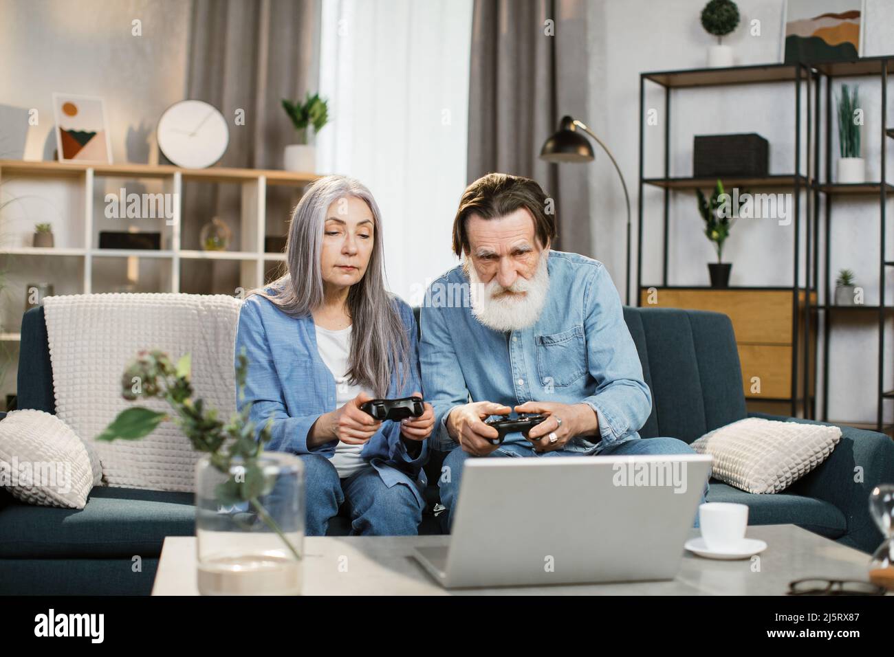 Joyful mature married couple with wireless joysticks in hands playing video games while sitting on comfy couch photo
