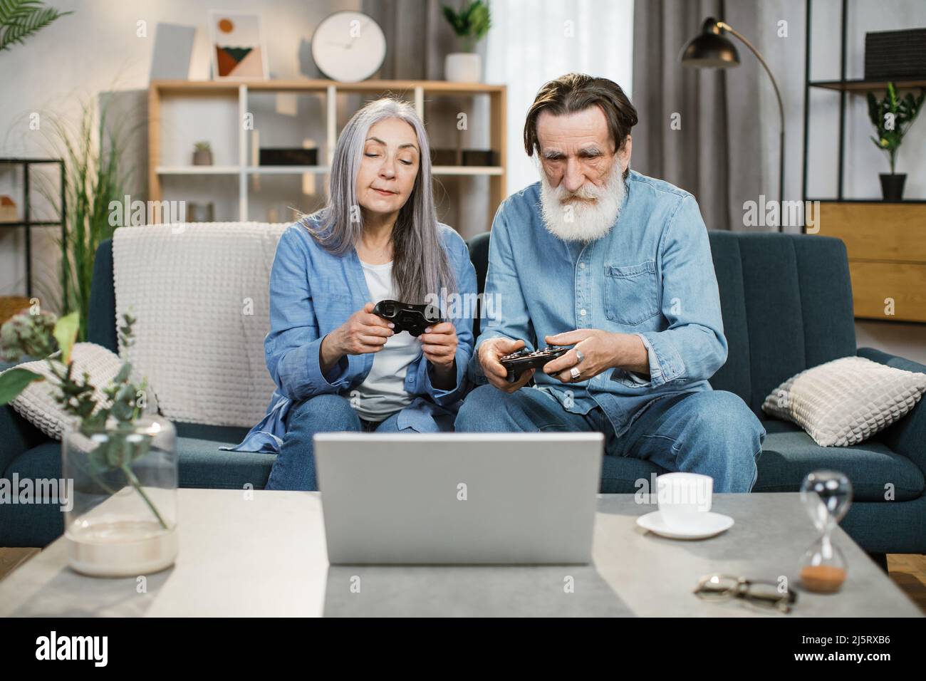 Joyful mature married couple with wireless joysticks in hands playing video games while sitting on comfy couch photo