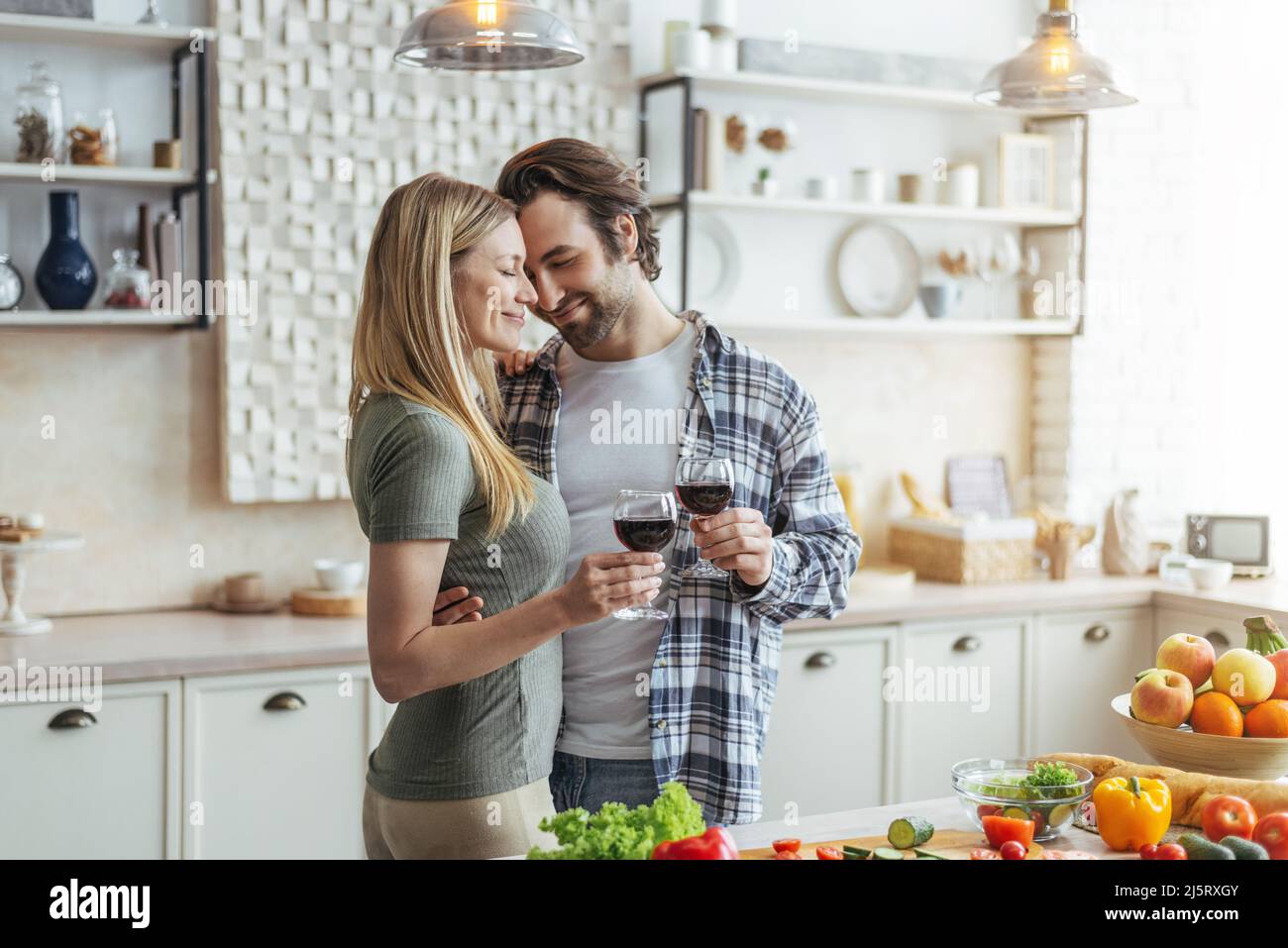 Smiling young european man with stubble and lady clinking glasses of wine, enjoy tender moment in kitchen Stock Photo