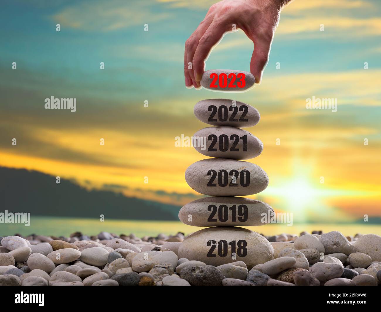 Happy new year 2023 concept. Entering the year 2023. Years ( 2018-2019-2020-2021-2022 ) written on the rising stone pile. Man hand adding stone to tow Stock Photo