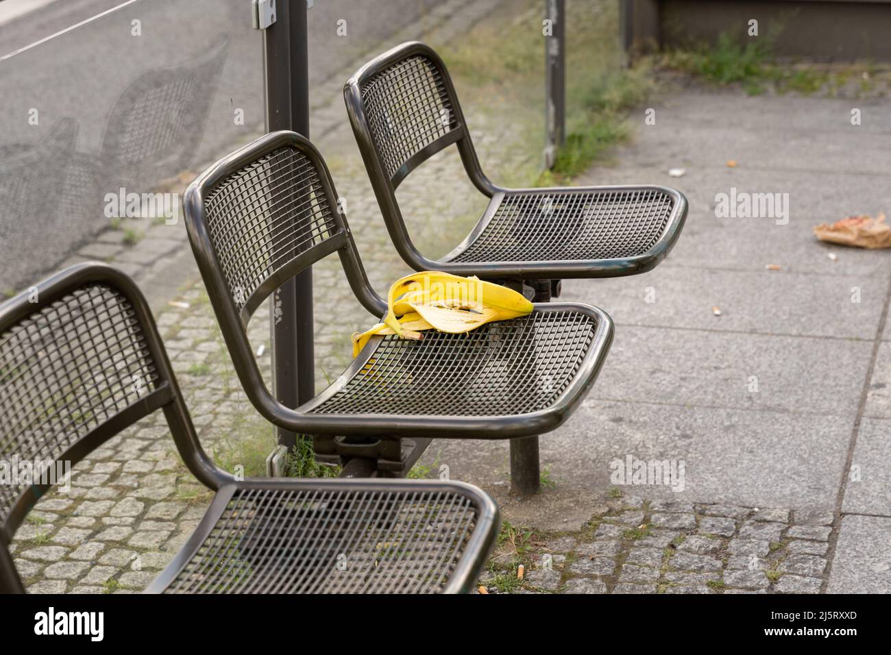 Banana peel waste on a seat at a bus stop. Pollution in an urban area. Dirty spot in a public area in a bus shelter. Organic trash lying around. Stock Photo