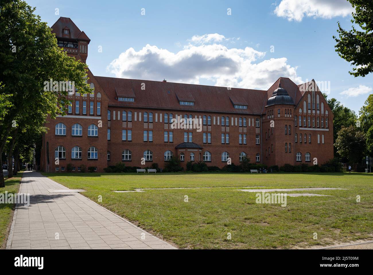 Hansa-Gymnasium in the town. Building of the Secondary school in an  old architecture. The house is built of red bricks. A place with grass in front. Stock Photo