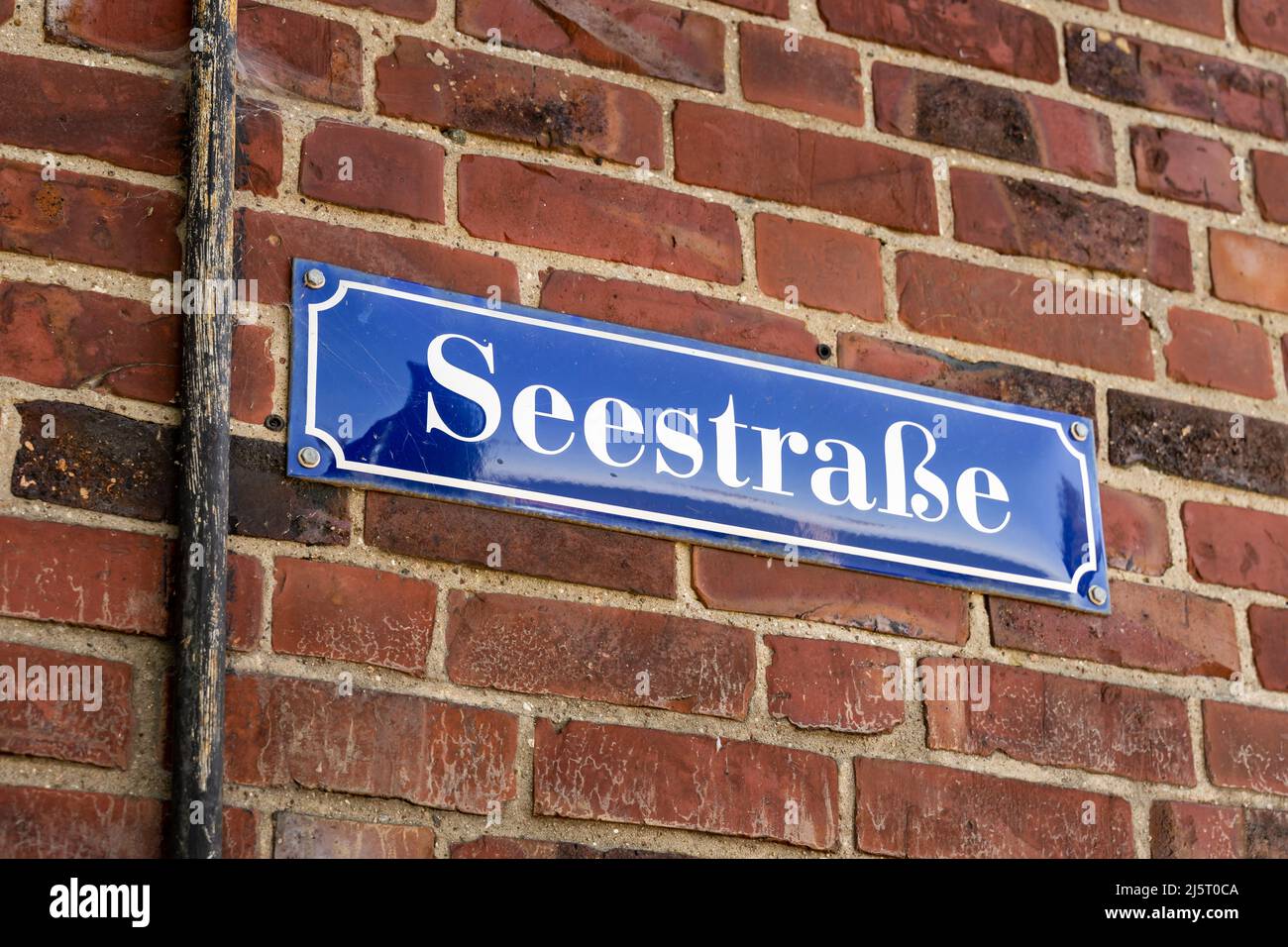 Seestrasse road sign on a red brick wall in Germany. White letters on a blue metal plate. Weathered grungy wall with dirt and cobwebs. Building Stock Photo