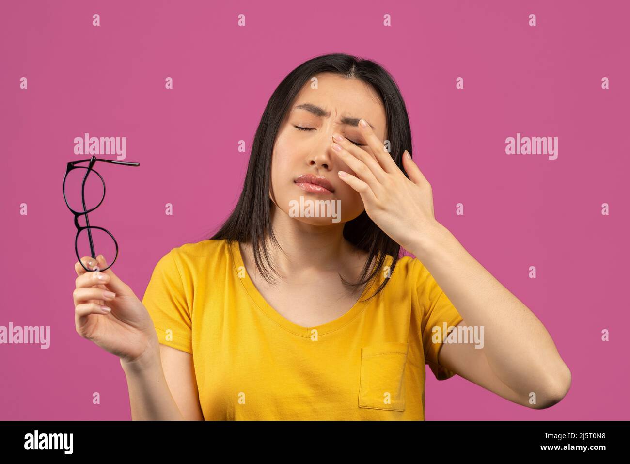 Young asian lady suffering from eye pain, taking off glasses and