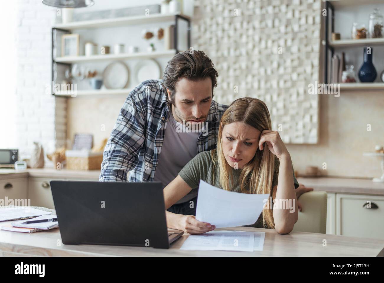 Unhappy young caucasian family think, look at document, pay bills and taxes at table with laptop Stock Photo