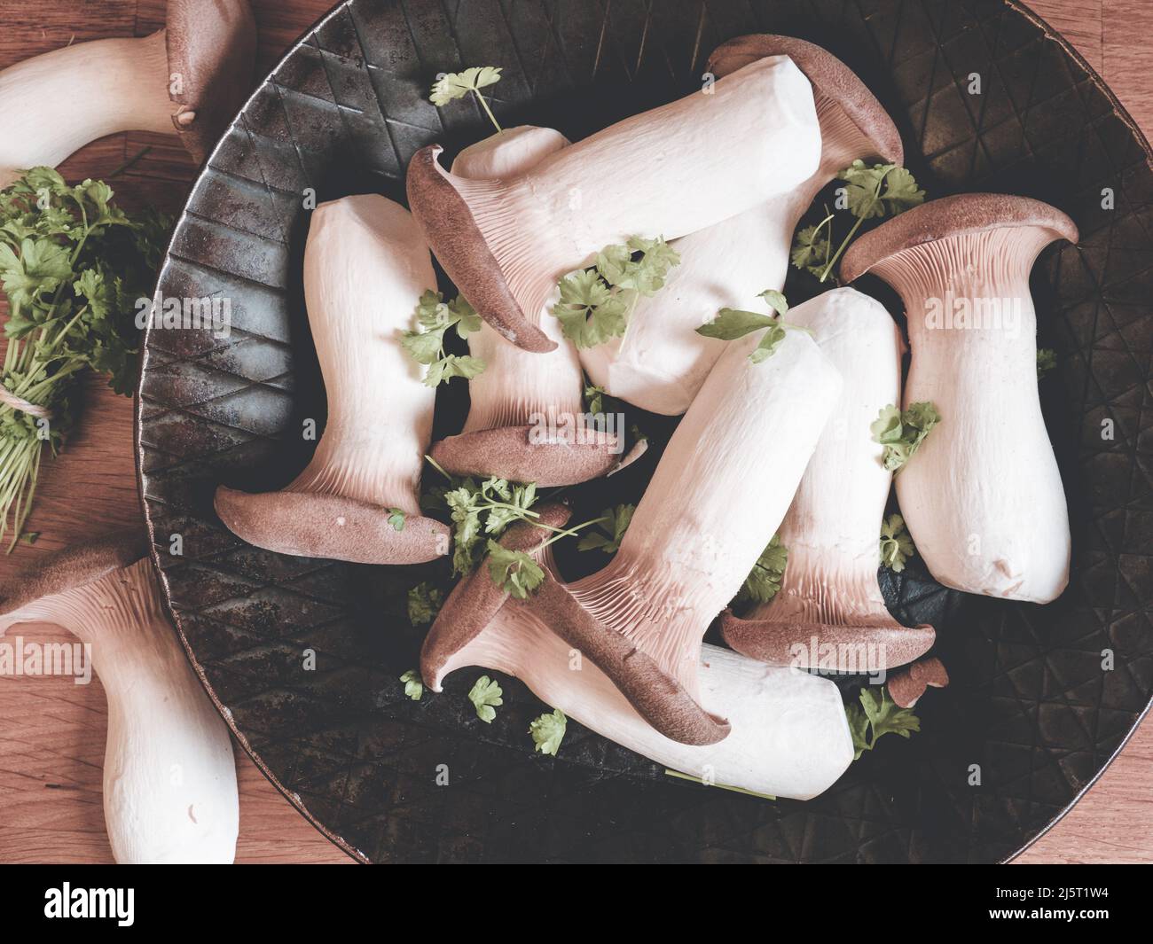 raw king oyster mushrooms on iron pan decorated with parsely - top view; on wooden kitchen board Stock Photo