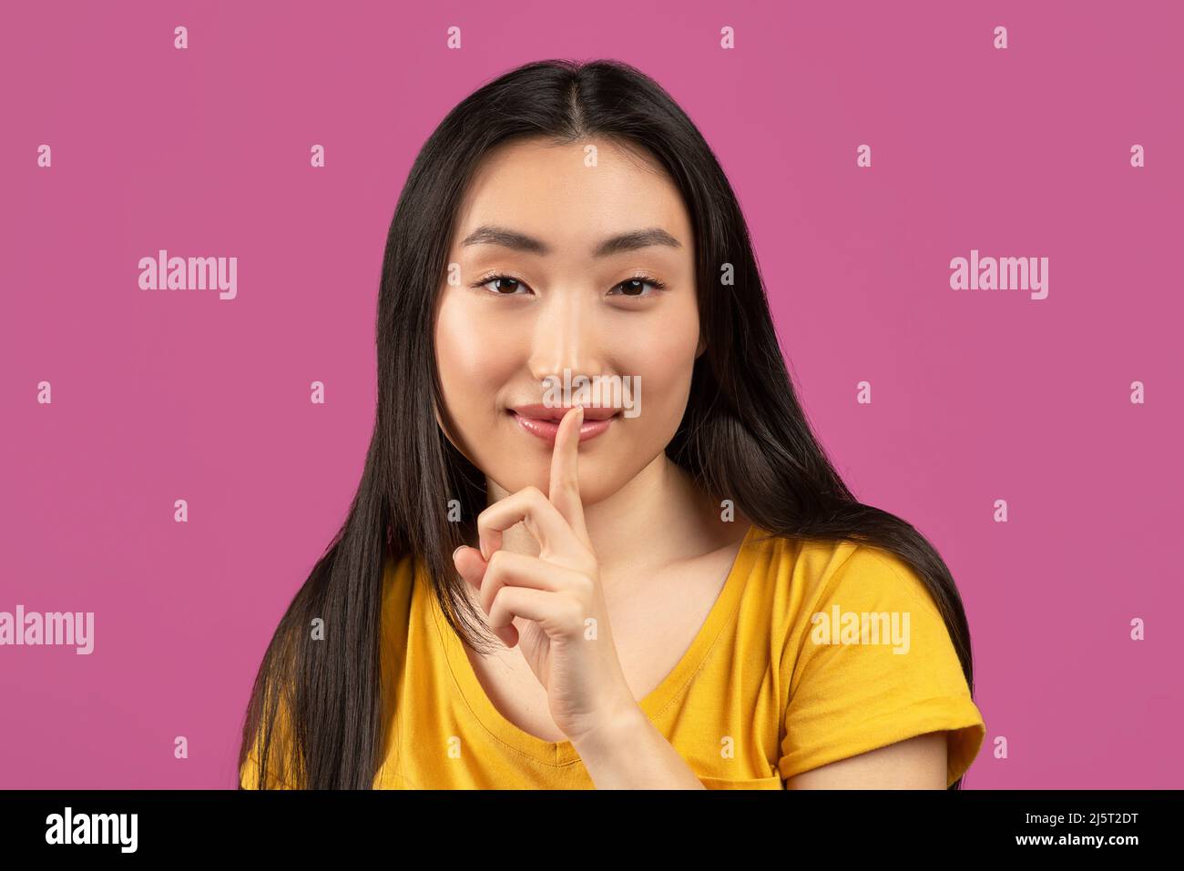 Mysterious asian lady holding finger near lips and looking at camera, pretty woman making shh gesture Stock Photo