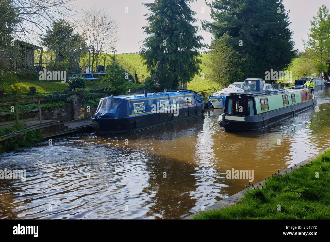 A narrow boat passing another moored one with other moored boats in the background on the Shropshire Union canal near Audlem, Cheshire, UK Stock Photo
