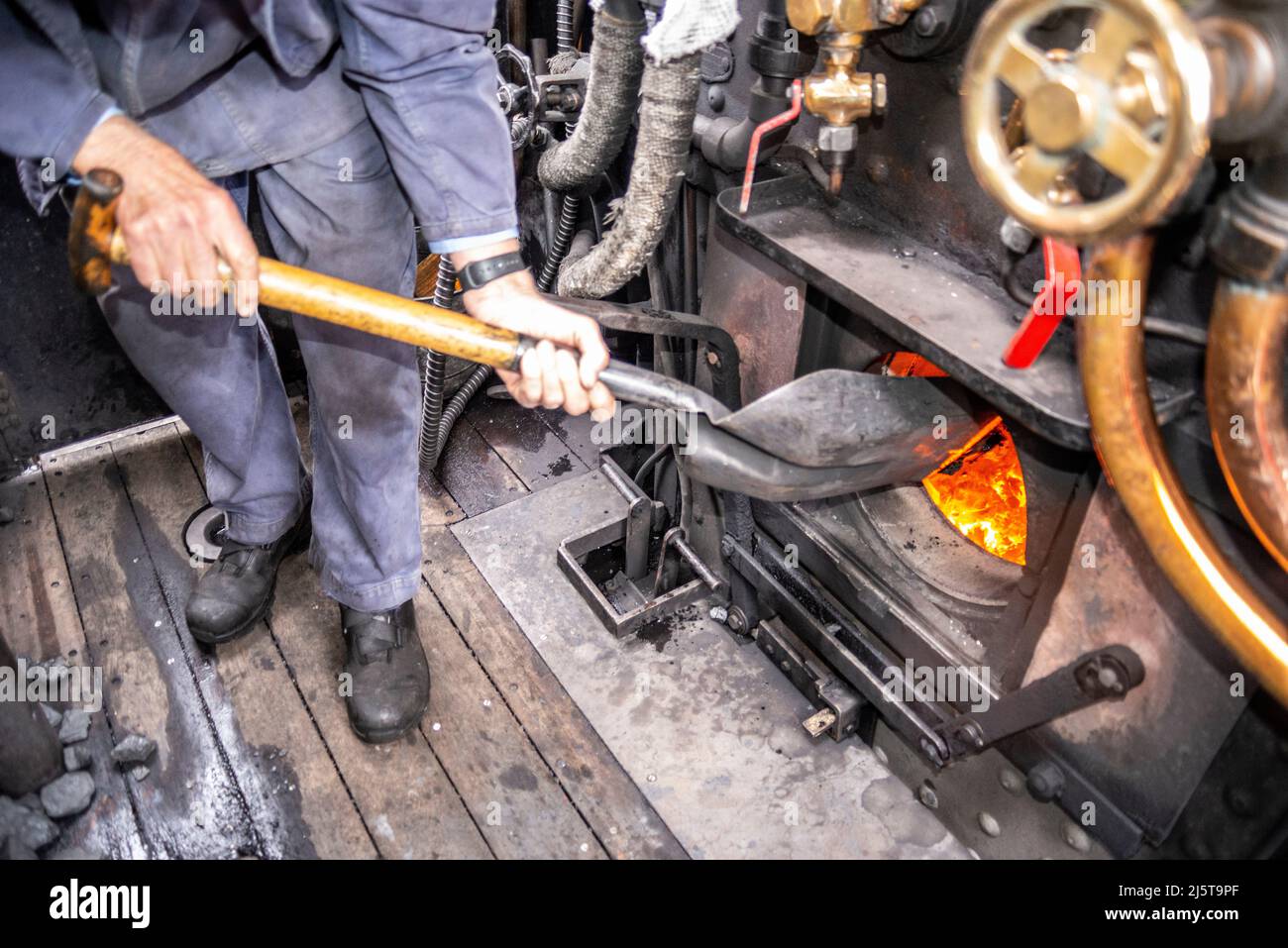 Coal being shovelled into the firebox of a steam locomotive. Engineer, driver, fireman in cab of Hunslet Austerity 0-6-0 feeding coal burning boiler Stock Photo