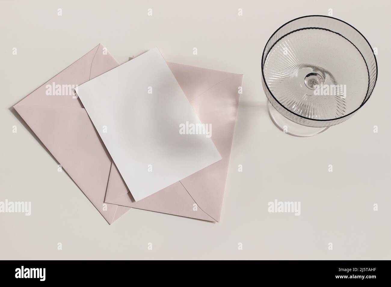 Modern summer stationery still life. Champagne, cocktail glass with long shadows. Blush pink envelopes, blank greeting card mock up scene. Beige table Stock Photo