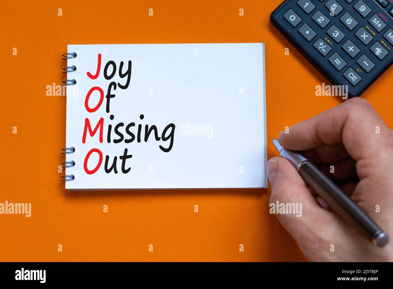 JOMO joy of missing out symbol. Concept words JOMO joy of missing out on the note on a beautiful orange background. Businessman hand. Calculator. Busi Stock Photo