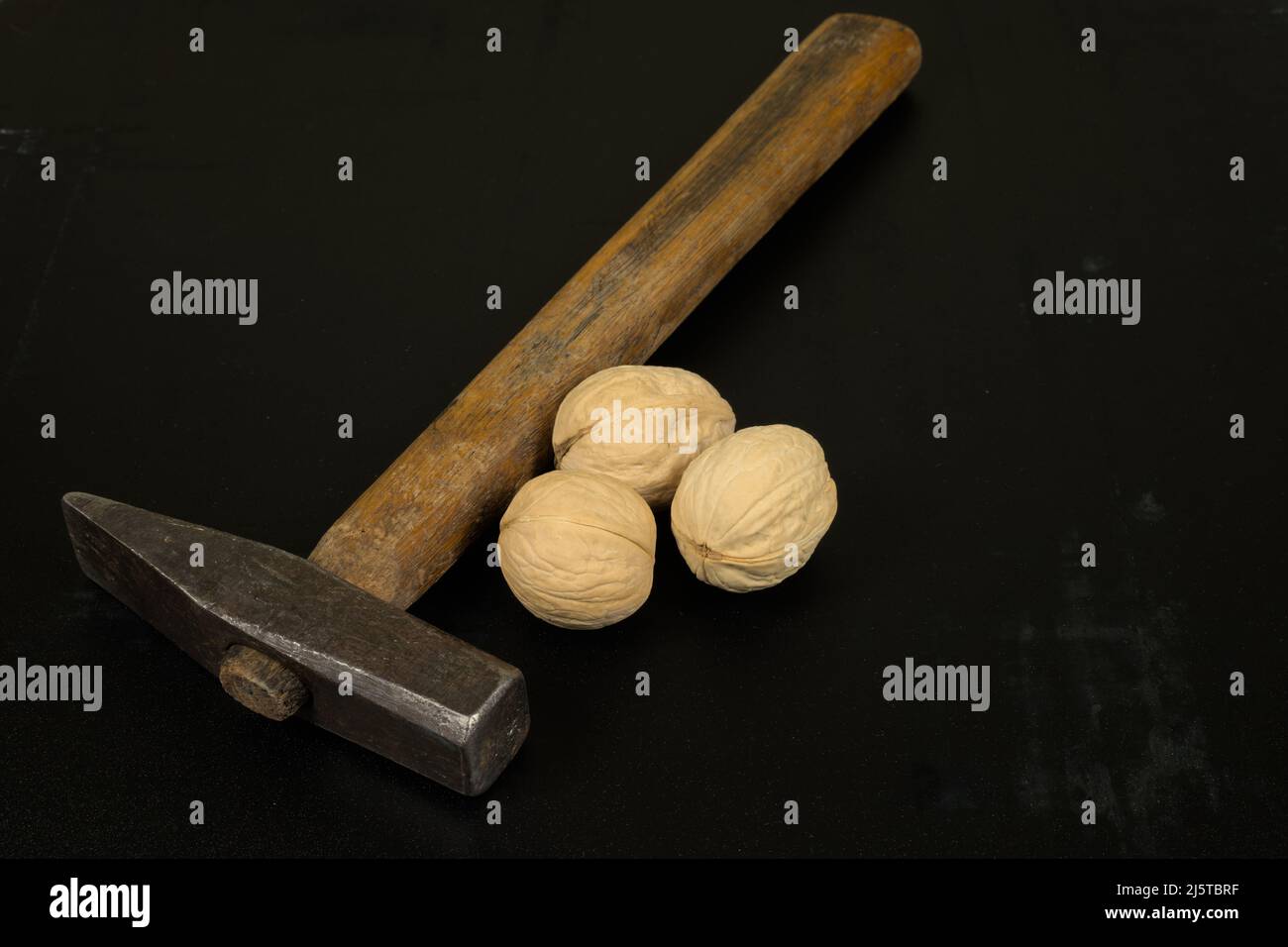 Three walnuts and a hammer on a dark scratched background Stock Photo