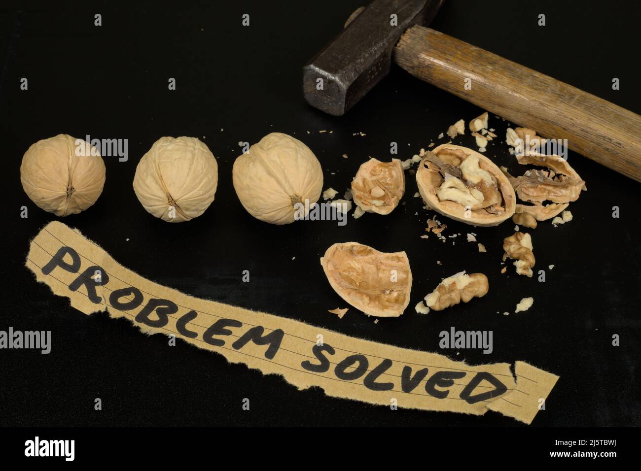 Four walnuts (one of them cracked) and a hammer on a dark scratched background (illustration of problem solving) Stock Photo
