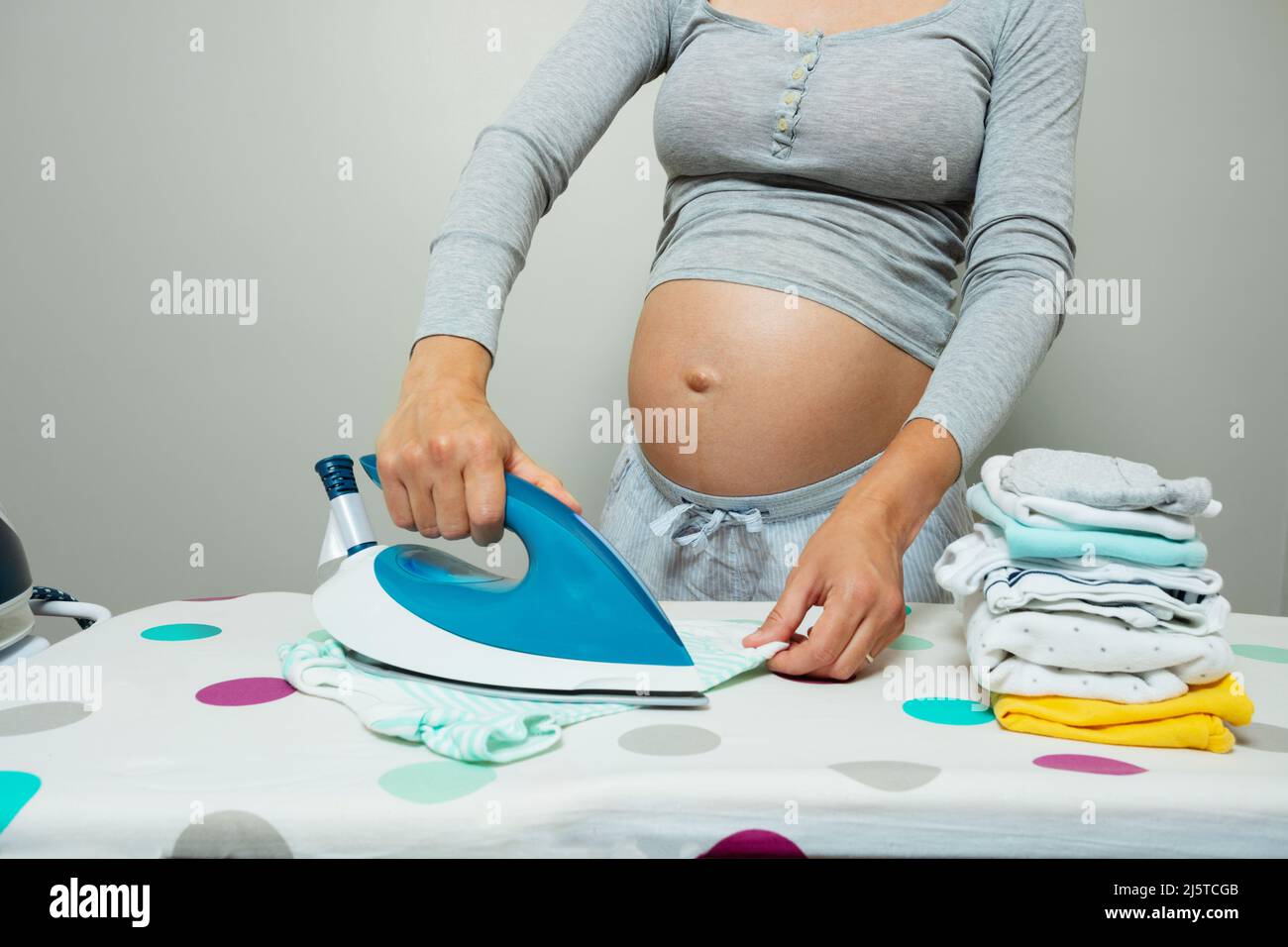 Pregnant woman's belly close up, ironing newborn clothes Stock Photo