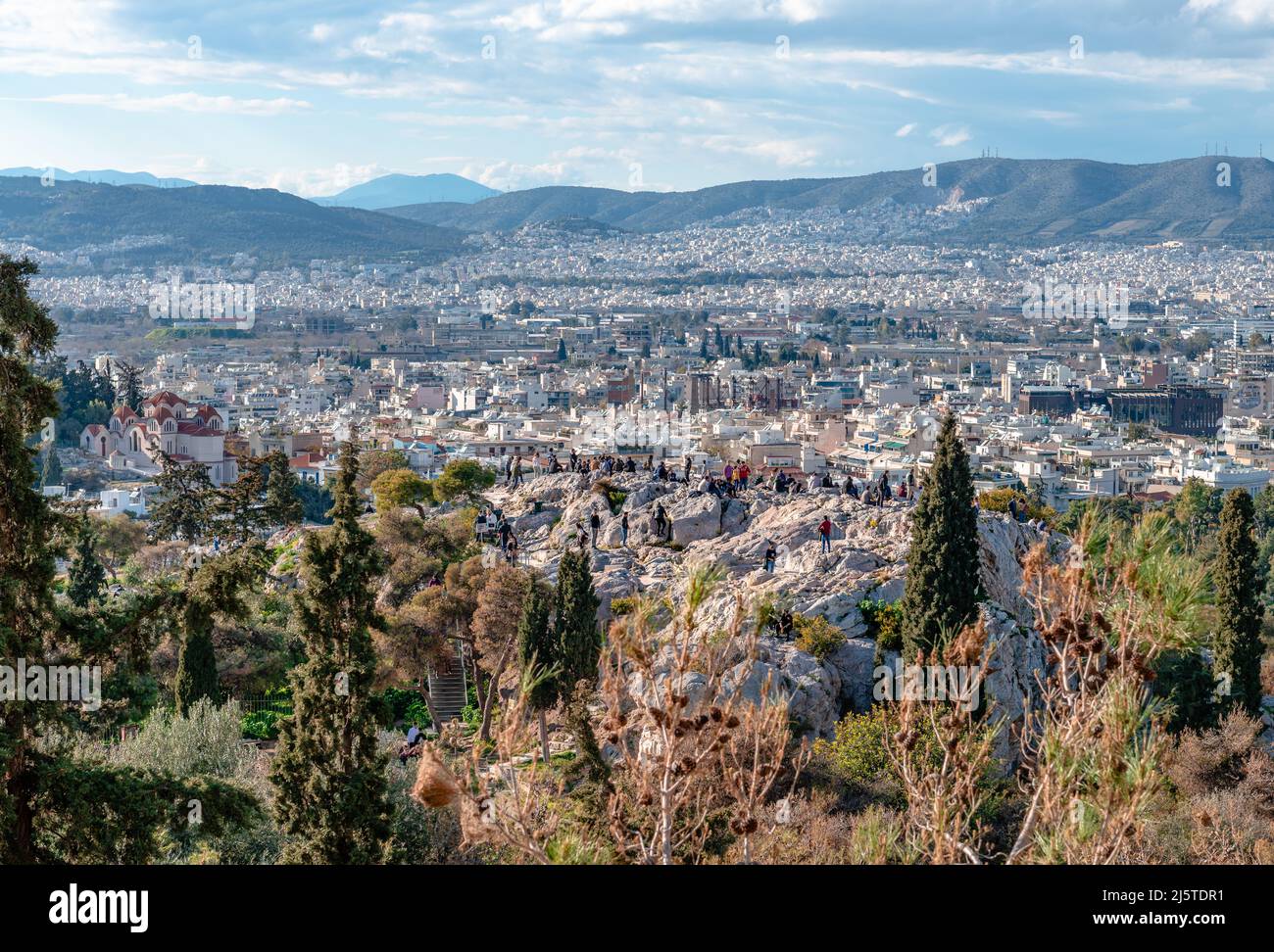 Athens, Greece - March 6 2022: Incidental people on the Areopagus Hill enjoy the skyline of Athens. Photo taken from the Acropolis Hill. Stock Photo