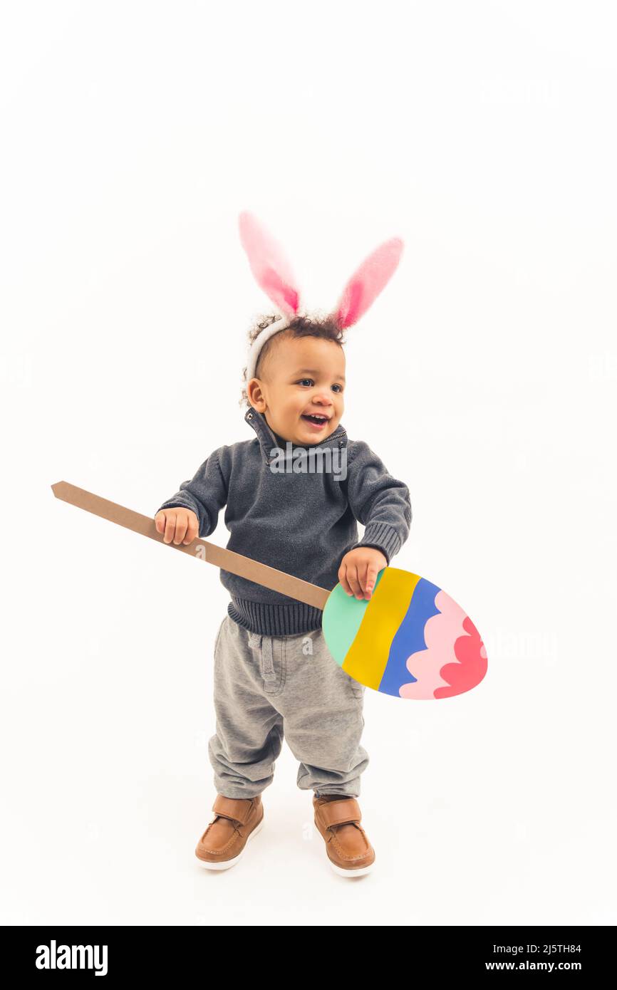 Small child holding cartoon Easter egg and wearingbunny ear looks happy and excited, fuul length. High quality photo Stock Photo