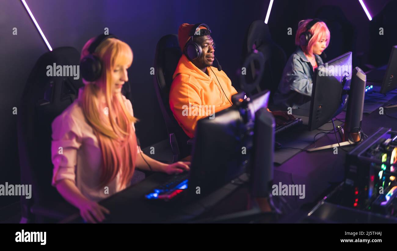 Online gaming team. Three interracial people sitting in an Internet cafe, playing on desktop computers, using professional headset. High quality photo Stock Photo