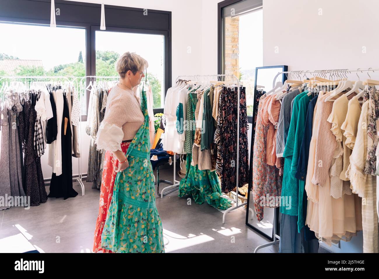 mature woman testing a dress in front of a mirror. blonde female shopping  in a fashion shop. shopping concept Stock Photo - Alamy