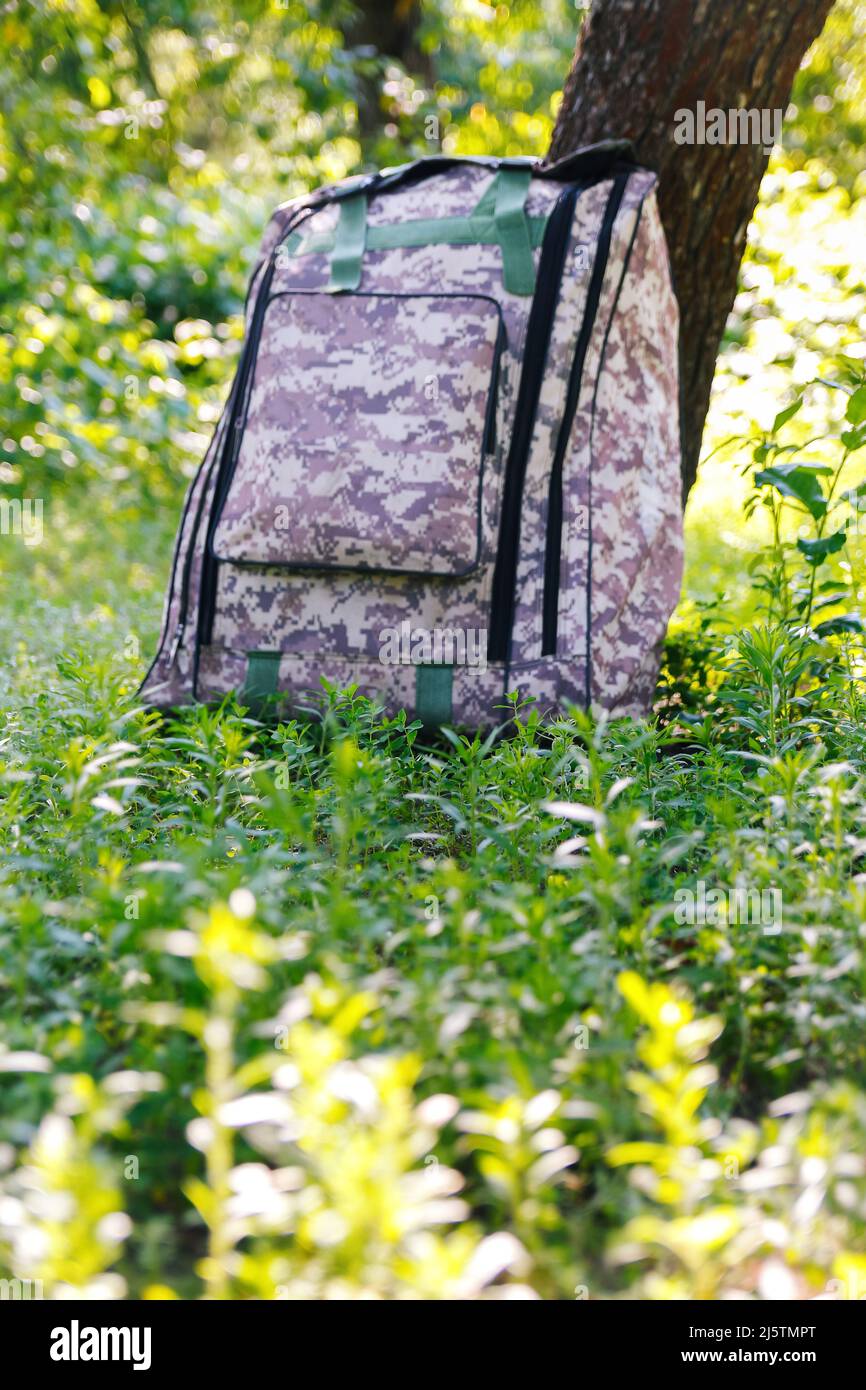 Defocus military backpack. Army bag on green grass background near tree