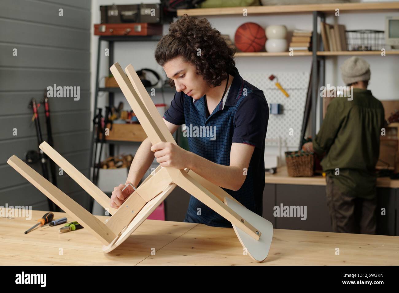 Contemporary teenage guy repairing or making wooden chair while