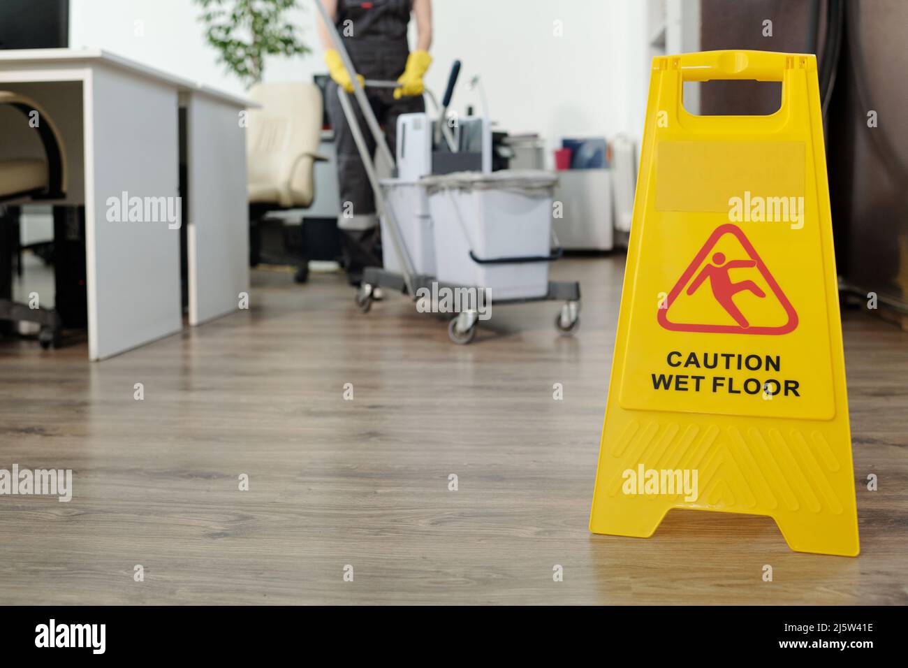 https://c8.alamy.com/comp/2J5W41E/caution-of-wet-floor-on-yellow-signboard-in-openspace-office-against-female-cleaner-pushing-janitor-cart-with-buckets-and-mop-2J5W41E.jpg