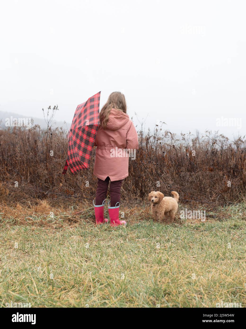 A young girl wearing rainboots and coat holding an umbrella look Stock Photo